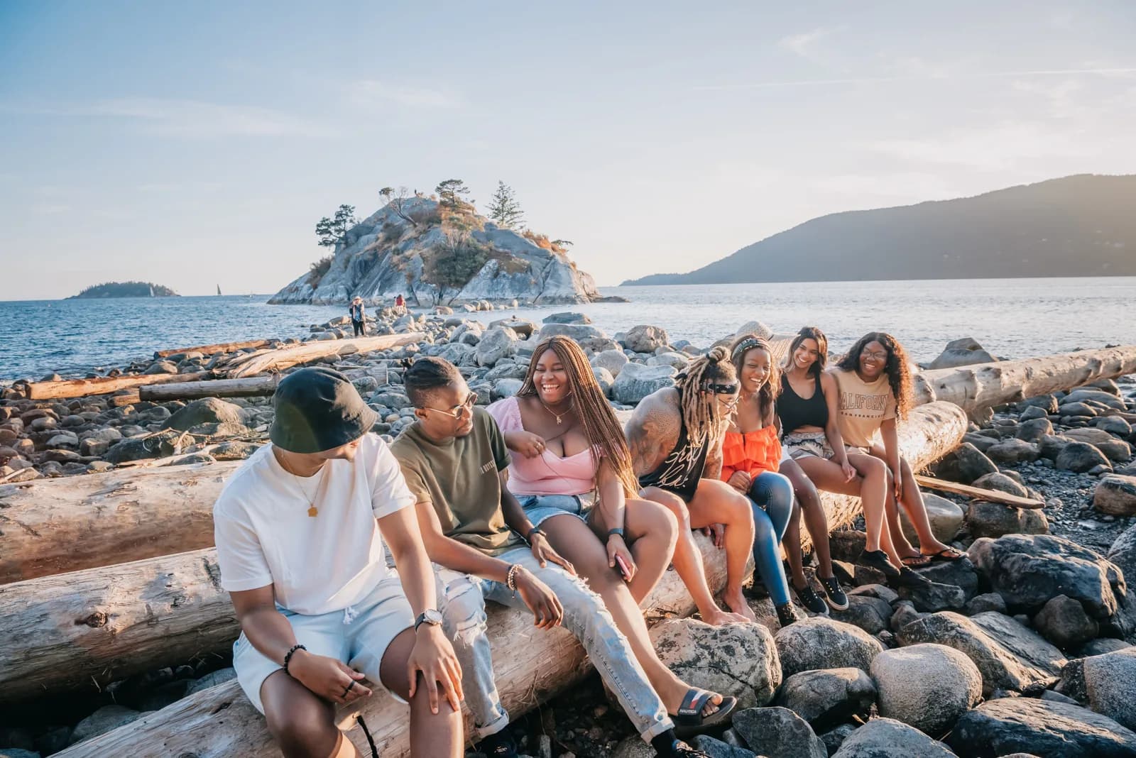 Friends laughing together on a driftwood log by the sea in evening light.